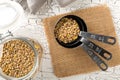 Raw, dry, uncooked brown lentil legumes in glass storage jar and measurement scoops on white wood table background flat lay top Royalty Free Stock Photo