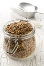 Raw, dry, uncooked brown lentil legumes in glass storage jar on white wood table background Royalty Free Stock Photo