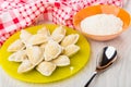 Raw dumplings on yellow plate, napkin, bowl with flour, spoon