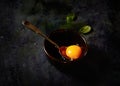 Raw egg in a bowl, spoon, basil on a black background