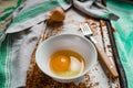 Raw egg broken into a white bowl with yolk and protein, next to the shell, fork and towel on a rusty metal background