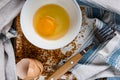 Raw egg broken into a white bowl with yolk and protein, next to the shell, fork and towel on a rusty metal background Royalty Free Stock Photo