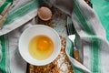 Raw egg broken into a white bowl with yolk and protein, next to the shell, fork and towel on a rusty metal background Royalty Free Stock Photo
