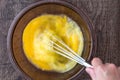 Raw eggs in glass bowl, womanÃ¢â¬â¢s hand with stainless steel whisk, whipping eggs, on a wood table