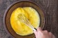 Raw eggs in glass bowl, womanÃ¢â¬â¢s hand with stainless steel whisk, whipping eggs, on a wood table