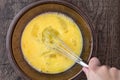 Raw eggs in glass bowl, womanÃ¢â¬â¢s hand with stainless steel whisk, whipping eggs, on a wood table