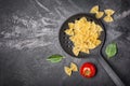 Raw farfalle pasta in black skimmer with basil and Cherry tomatoes