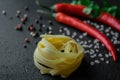 Raw fettuccine paste on black background with chili fresh cilantro twigs sea salt and peppercorns