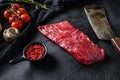 Raw, flap or flank, also known Bavette steak near butcher knife with pink pepper and rosemary. Black stone background. Side view