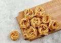 Raw flat long shaped pasta tagliatelle on a wooden cutting board on a light gray background