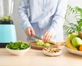 Raw foodism, green smoothie with vegetables and fruits. Woman cutting kiwi and banana to blender