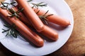 Raw frankfurter sausage with rosemary in plate on wooden table. Fresh pork meat wiener closeup Royalty Free Stock Photo