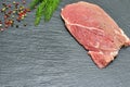 Raw fresh beef meat on a black background with a sprig of dill and peppercorns
