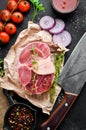 Raw fresh cross cut veal shank for makin Osso Buco with spgices and herbs on a black background.