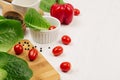 Raw fresh green greens, red cherry tomatoes in bowl and kitchenware on soft white wood board, border. Spring vitamin dieting food.