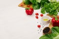 Raw fresh green vegetables, greens, red cherry tomatoes and kitchenware on soft white wood board, border. Royalty Free Stock Photo