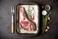 Raw fresh Lamb Meat in baking tray, herbs and fork on black stone background. Royalty Free Stock Photo