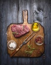 Raw fresh marbled beef steak with meat fork and seasonings on rustic cutting board over blue wooden background