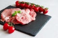 Raw fresh pork steaks with a sprig of basil and cherry tomatoes on a branch lie on a black stone cutting board. Preparing meat for Royalty Free Stock Photo