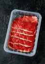 Raw fresh sizzling beef steak slices in plastic tray in butcher`s shop on dark background table