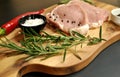 Raw fresh uncooked sliced pork fillet dish with rosemary, pepper, salt, red chili pepper on wooden board and black background. Royalty Free Stock Photo