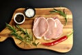 Raw fresh uncooked sliced pork meat fillet dish with rosemary, pepper, salt, red chili pepper on wooden board and black background Royalty Free Stock Photo