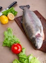 Raw fresh unprepared salmon fish on a wooden board with ingredients for cooking. Lemon, lettuce, tomatoes.