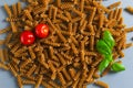 Raw fusilli pasta lie in a heap with cherry tomatoes and a sprig of basil on a gray background. Royalty Free Stock Photo