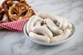 Raw German Bavarian WeiÃÅ¸wurst white sausage chain on plate and chives and butter pretzels in basket on marble background