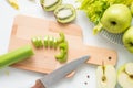 Raw green ingredients for smoothie, whole and cut apples, chopped celery stalk on a wooden board on white cloth background Royalty Free Stock Photo