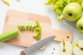 Raw green ingredients for smoothie, whole and cut apples, chopped celery stalk on a wooden board on white cloth background Royalty Free Stock Photo