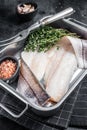 Raw haddock fish fillets, whitefish meat in kitchen tray with thyme. Black background. Top view