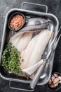 Raw haddock fish fillets, whitefish meat in kitchen tray with thyme. Black background. Top view