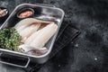 Raw haddock fish fillets, whitefish meat in kitchen tray with thyme. Black background. Top view. Copy space