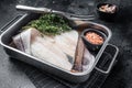 Raw haddock fish fillets, whitefish meat in kitchen tray with thyme. Black background. Top view