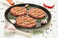 Raw hamburgers - cutlets from organic beef meat with garlic, chilli and rosemary in a frying pan on a white background Royalty Free Stock Photo