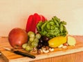 Healthy raw vegetables, fruits, lettuce, nuts and red peppers on a wooden plate