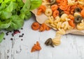 Raw homemade tricolore trottole pasta in brown paper on white wooden background with basil