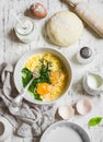 Raw ingredients for baking a pie with spinach - eggs, cheese, dough, spinach, cream on light wooden background.