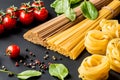 Raw italian pasta.Spaghetti and fettuccine with tomatoes, herbs and pepper on a black background. Closeup. Royalty Free Stock Photo