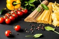Raw italian pasta.Spaghetti and fettuccine with tomatoes, vegetables, herbs and pepper on a black background . Closeup. Royalty Free Stock Photo
