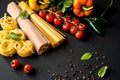 Raw italian pasta.Spaghetti and fettuccine with tomatoes, vegetables, herbs and pepper on a black background . Closeup. Royalty Free Stock Photo