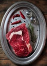 Raw juicy beef steak with rosemary, salt, pepper and chili pepper on an iron plate on the wooden table Royalty Free Stock Photo