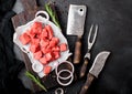 Raw lean diced casserole beef pork steak with vintage meat hatchet and fork with knife on stone background. Rosemary with red