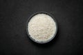 Raw long grain rice in black ceramic bowl on dark slate table top. Heap of uncooked basmati or jasmine rice Royalty Free Stock Photo