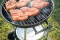 Raw marinated pork neck steak meat roasting on kettle barbecue grill with charcoal and smoke in garden on summer evening Royalty Free Stock Photo