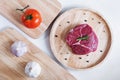 Raw meat, beef steak, on wooden board with tomato and garlic. Top view Royalty Free Stock Photo