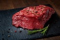 Raw meat beef steaks on black slate board with spices and rosemary over wooden background, copy space Royalty Free Stock Photo