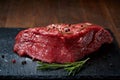 Raw meat beef steaks on black slate board with spices and rosemary over wooden background, copy space Royalty Free Stock Photo