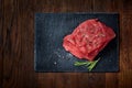 Raw meat beef steaks on black slate board with spices and rosemary over wooden background, copy space Royalty Free Stock Photo